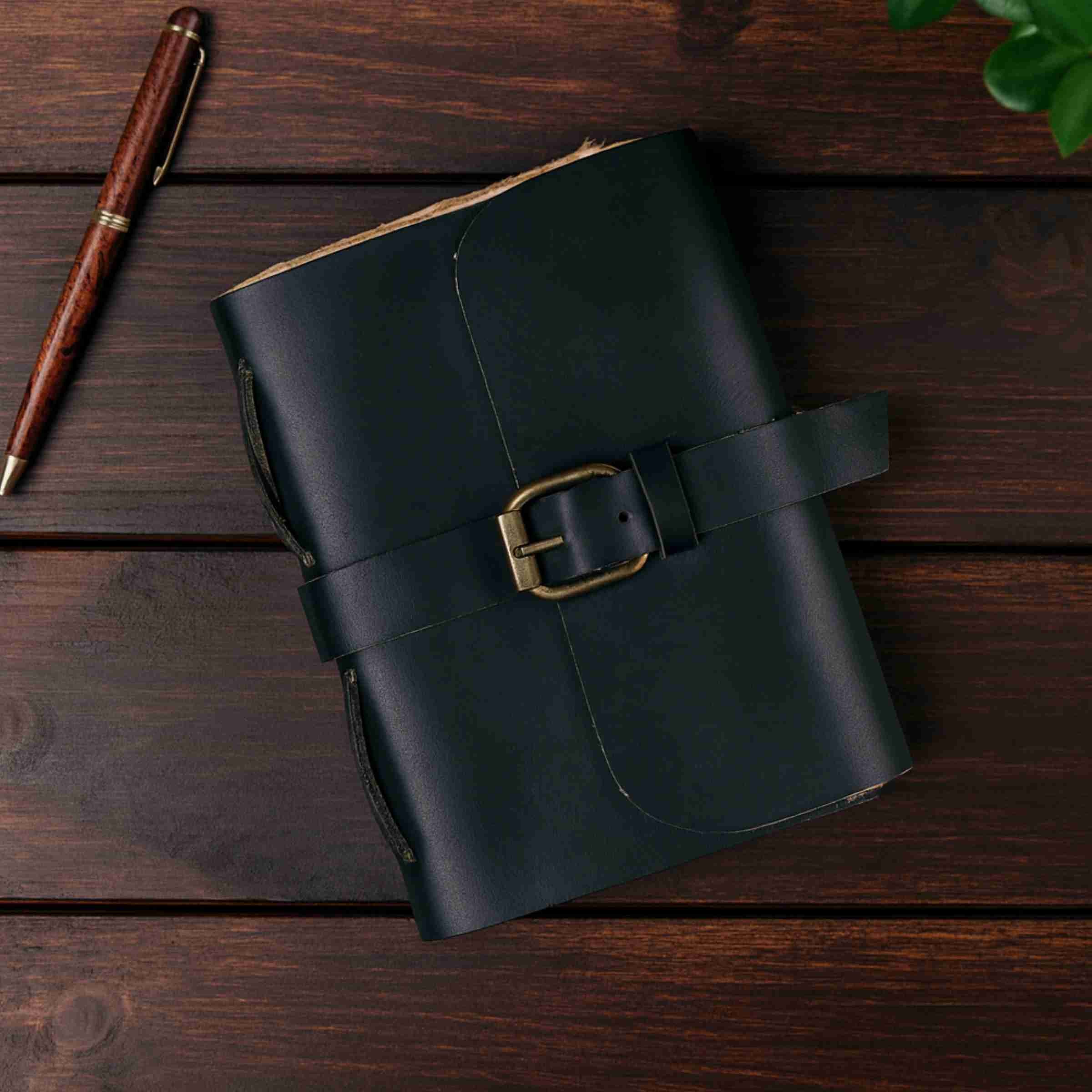 Black leather notebook with a gold buckle on a wooden surface, accompanied by a wooden pen.