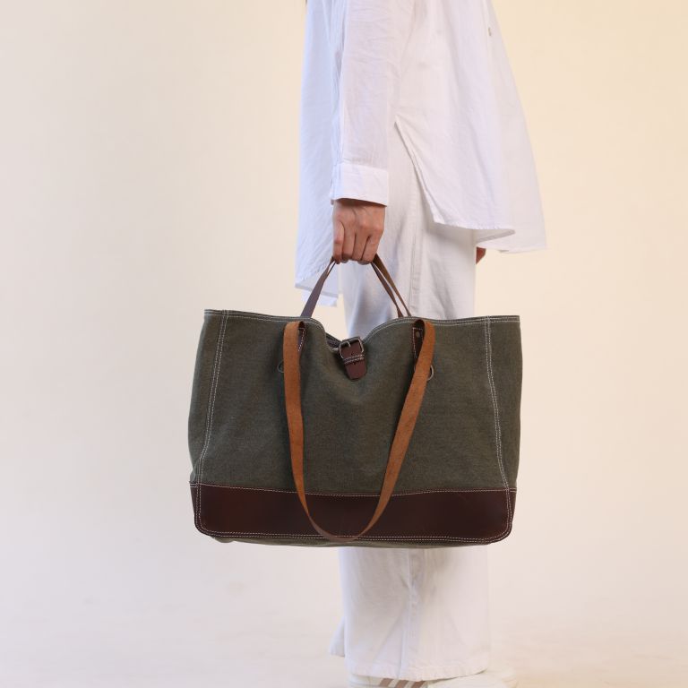 Person holding a green tote bag with brown accents against a plain background