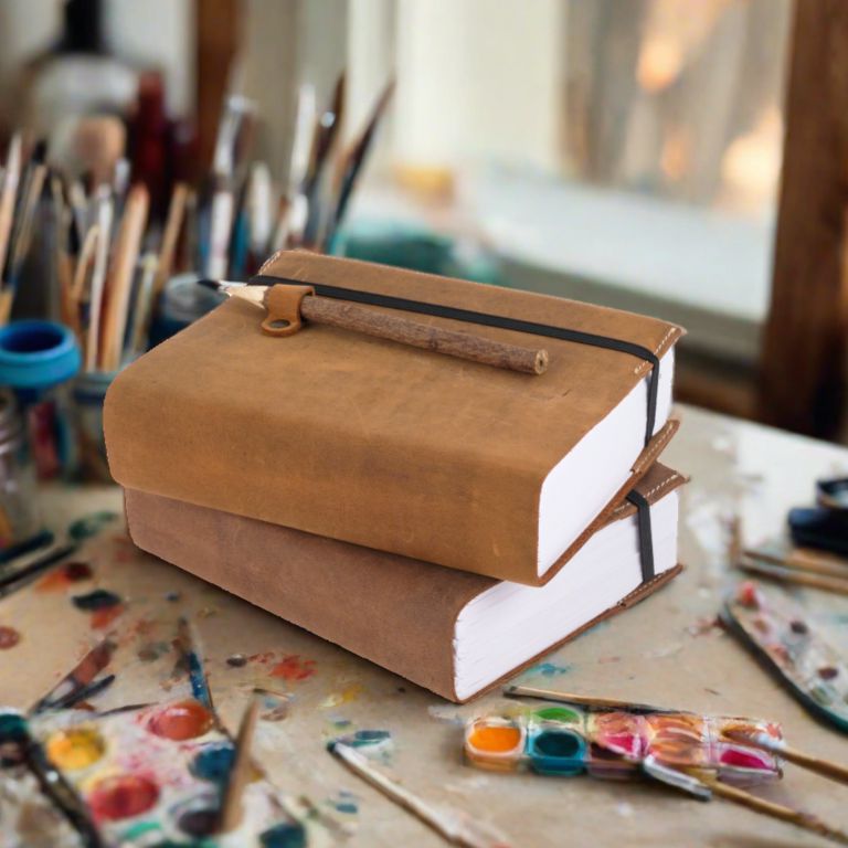 Stack of brown leather-bound books on a table with art supplies in the background