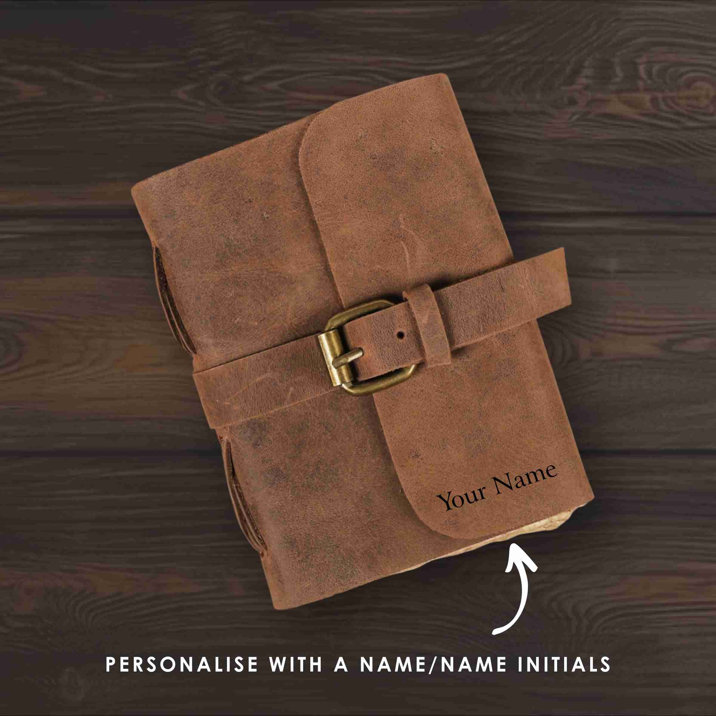 Brown leather notebook with a buckle on a wooden surface, personalized with 'Your Name'.