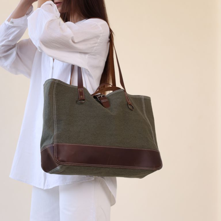 Person holding a green tote bag with brown accents against a beige background