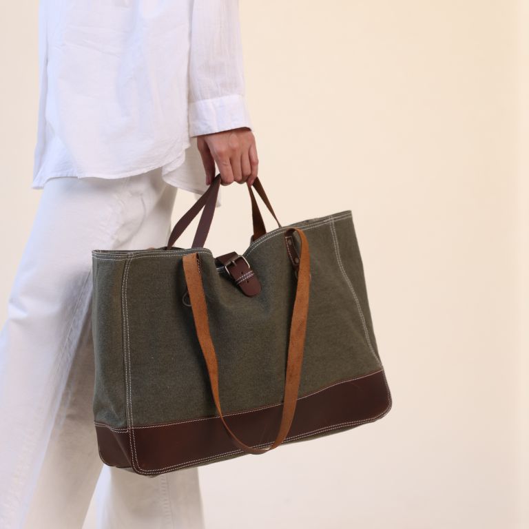 Person holding a green tote bag with brown accents on a beige background