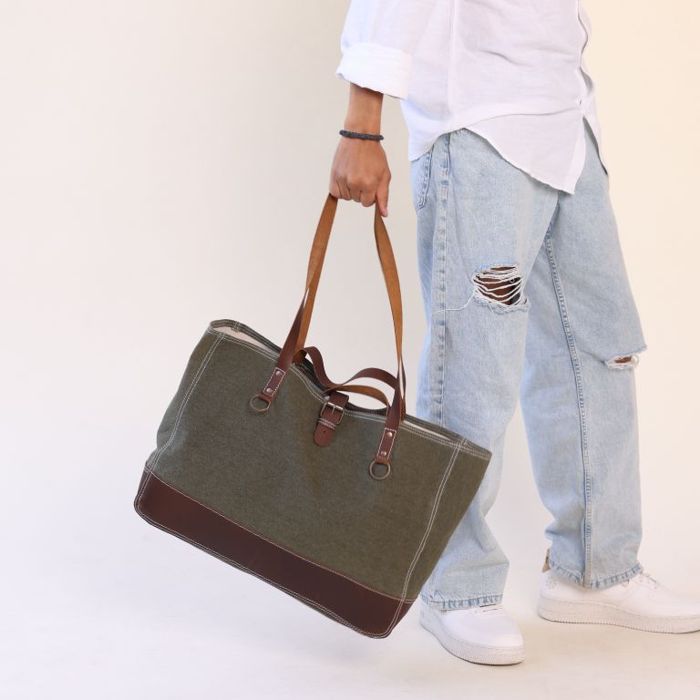 Person holding a green tote bag with brown handles against a plain background