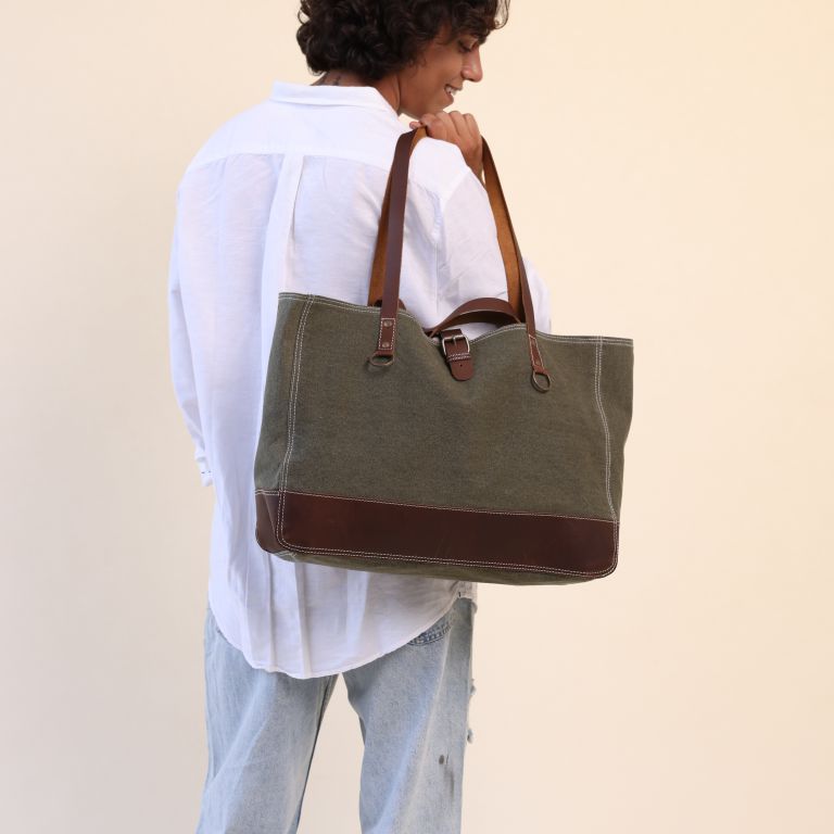 Person carrying a green tote bag with brown accents on a beige background