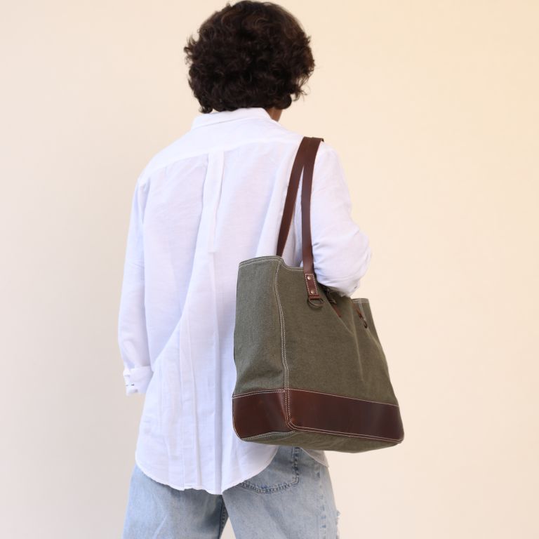 Person wearing a green tote bag with brown accents on a plain background