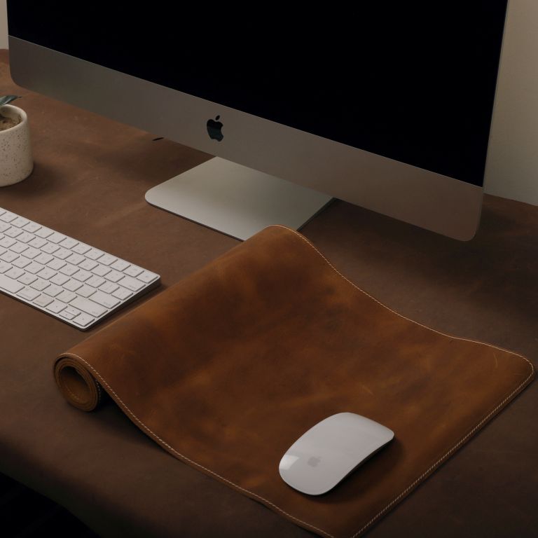 Brown leather mouse pad with a computer mouse on a wooden desk.