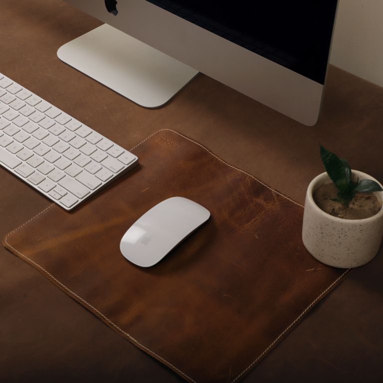Wooden desk with computer monitor, keyboard, mouse, and small plant on a wooden surface.