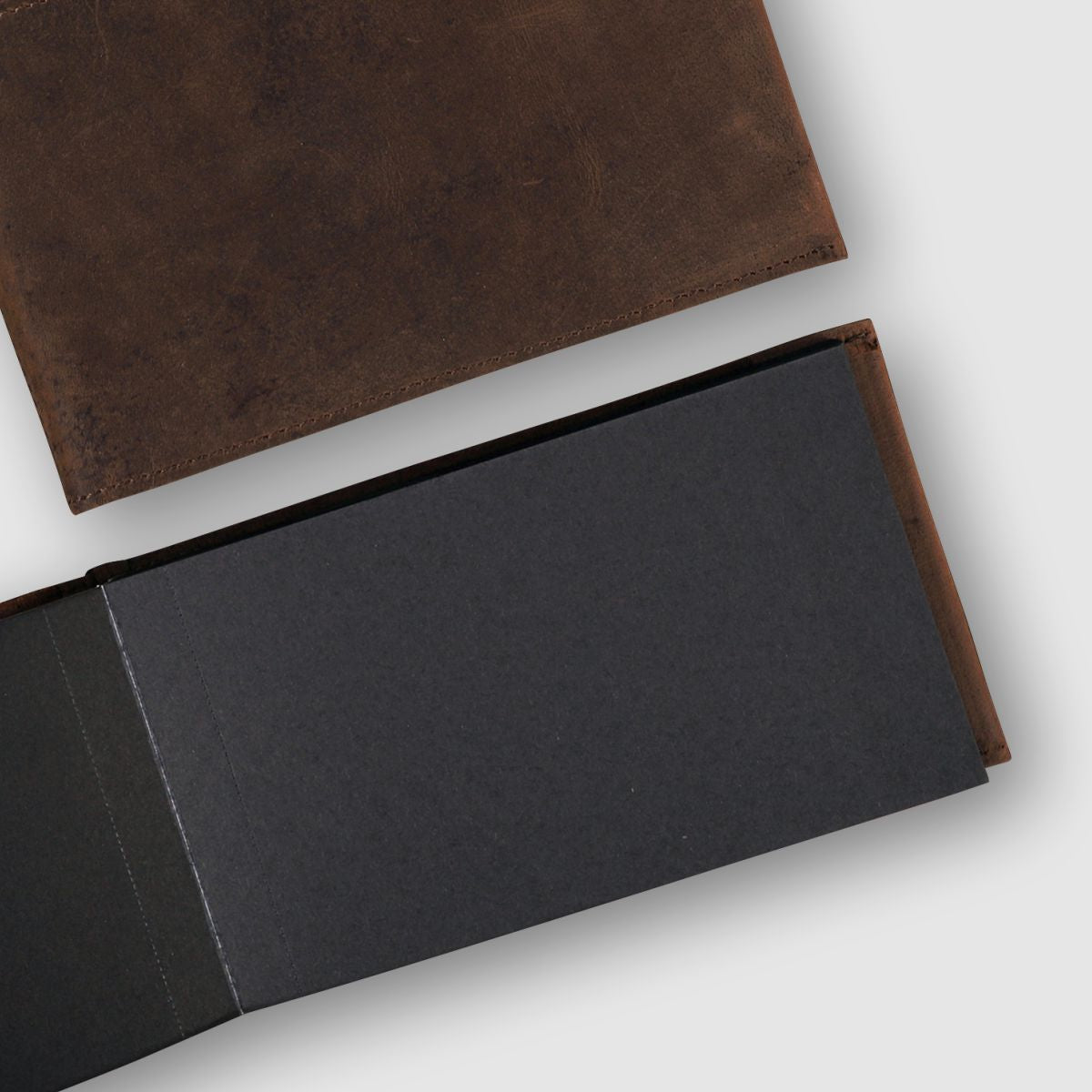 Black leather-bound book with a brown leather cover on a light gray background