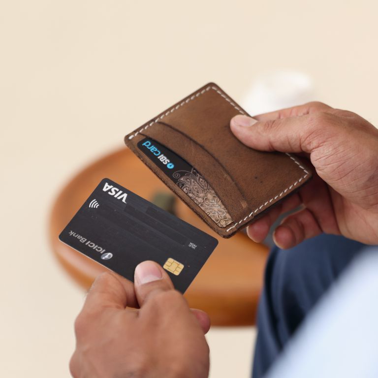 Person holding a brown wallet and a black card with Visa logo.