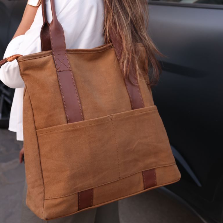 Brown tote bag with brown straps held by a person, blurred background