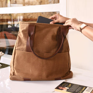 Person placing a tablet into a brown tote bag with leather handles, demonstrating its functionality and spaciousness