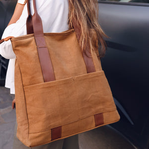 Woman carrying a brown tote bag with leather handles, showcasing its stylish design and spacious exterior pockets