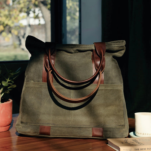 Olive green tote bag with leather handles on a table with books and a cup, perfect for daily use